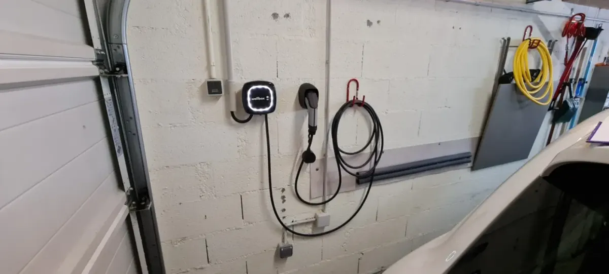 Borne de recharge murale posée dans un garage, avec un cheminement de câble soigné jusqu'au tableau